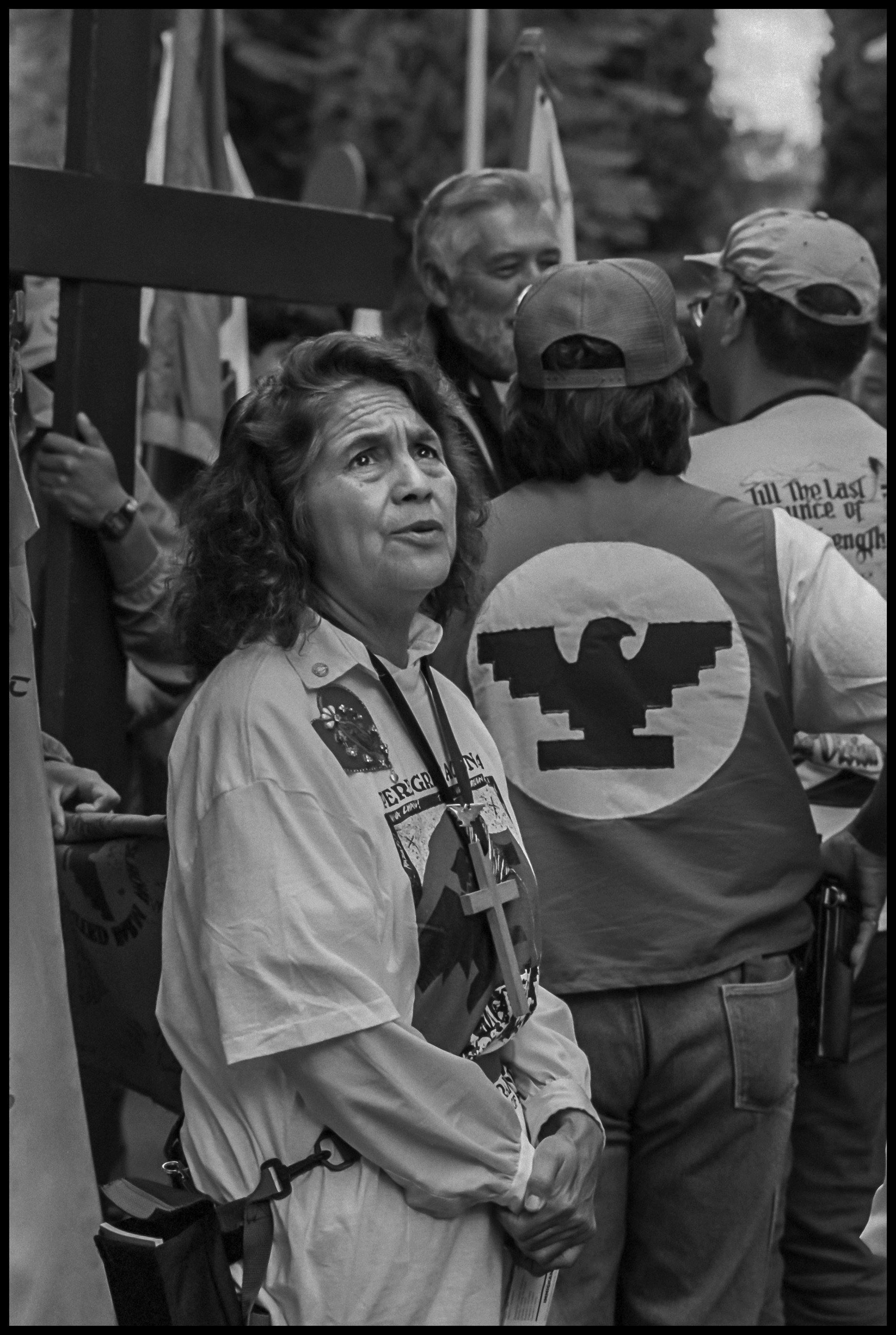 A tired Dolores Huerta standing in front of four other people and gazing up, as the march in Sacramento reaches its end after a month. 1994. The David Bacon Archive, Department of Special Collections, Stanford Libraries