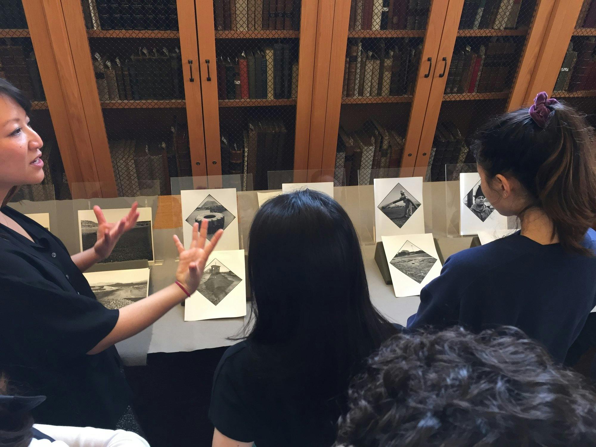 Professor Marci Kwon and a group of students stand in front of a series of Ruwedel's photographs on display, in front of cabinets of books.