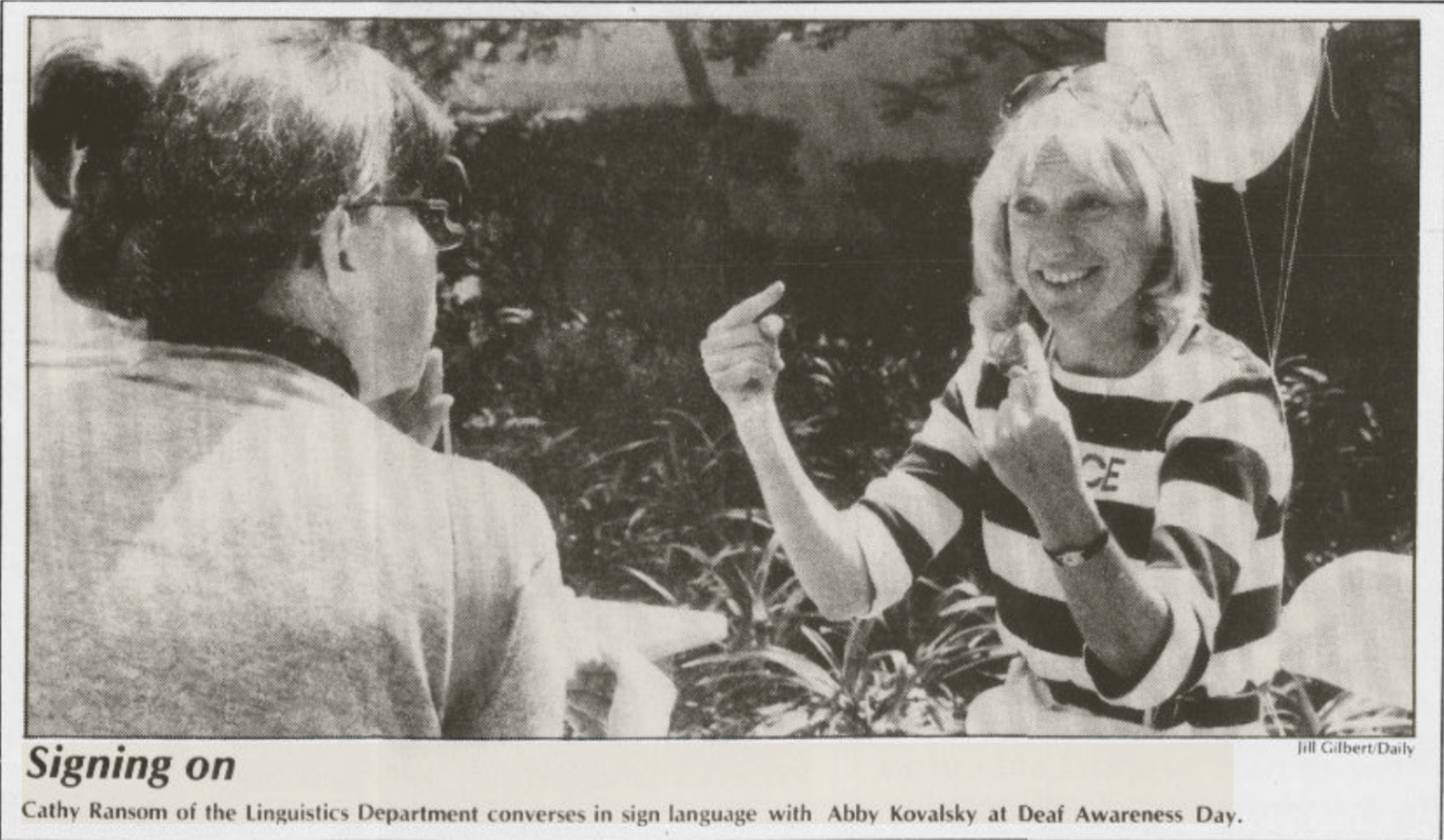 A  newspaper clipping of two women seated outside conversing in sign language.