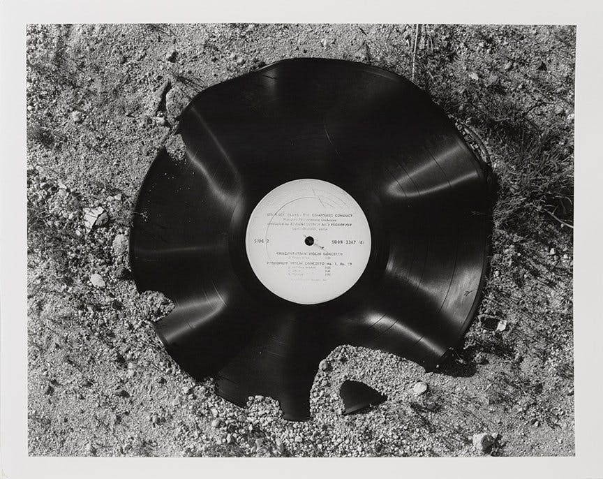 A warped vinyl record laying in dirt and sand.