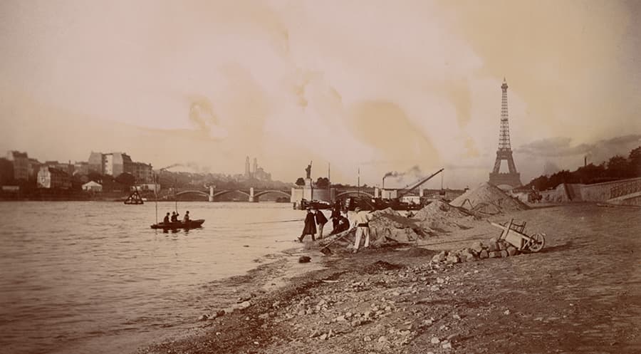 A photograph of Paris from the 1800s showing the Seine River with the Eiffel Tower in the background.