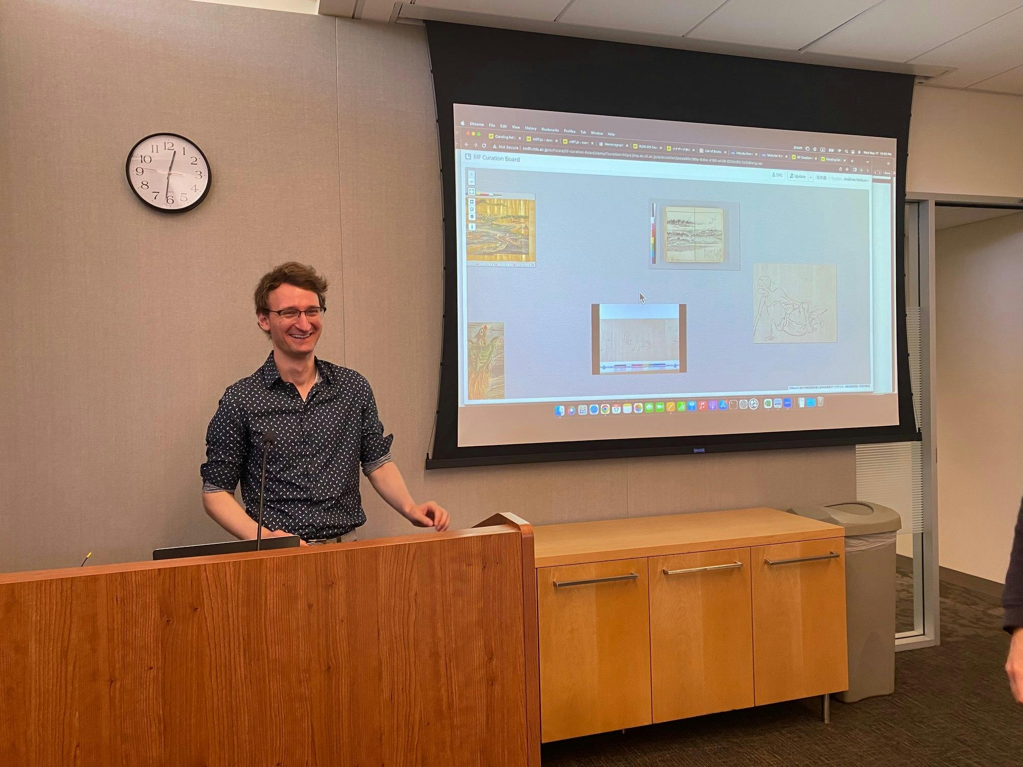 Andrew P. Nelson standing at a podium with a presentation on large screen.