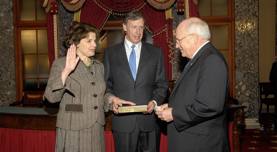 Three people standing at a swearing-in ceremony, the honoree with her hand on a book and the other raised.