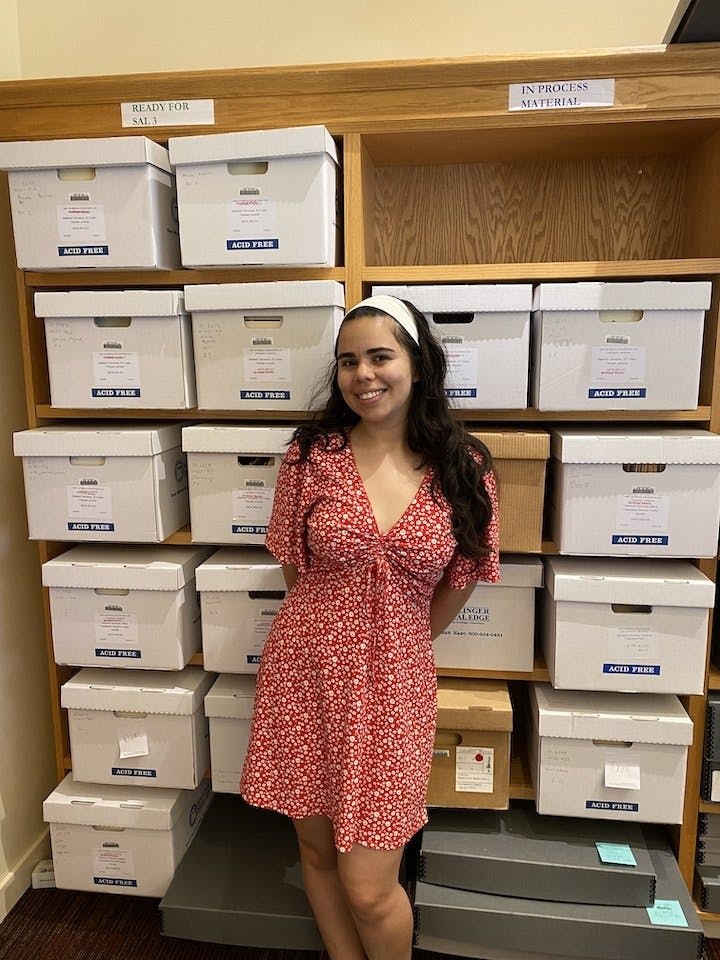 University Archives student intern, Stephanie Castaneda Perez, standing in front of numerous boxes of archival material.