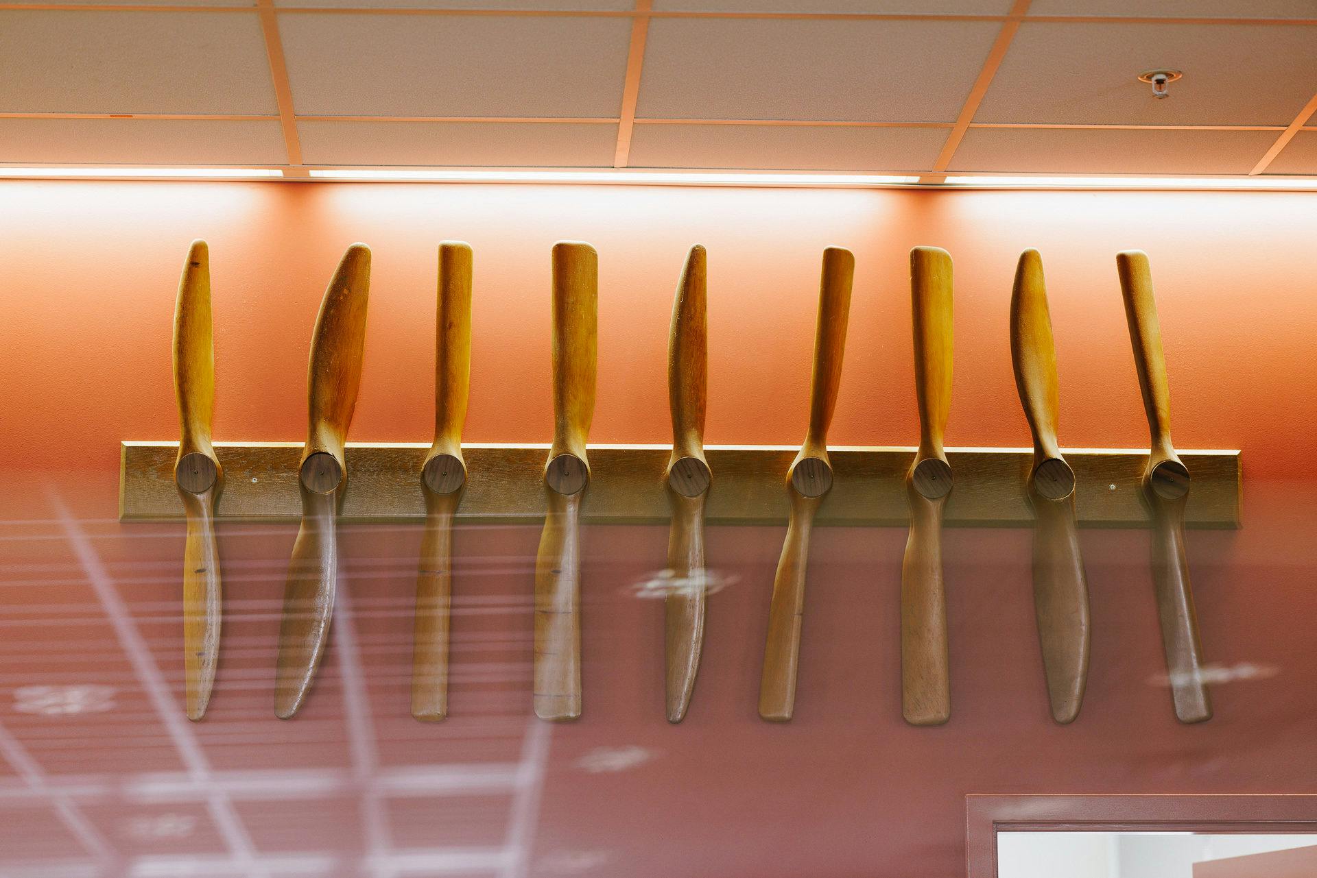 Nine wooden propellers on a wall mounted display.