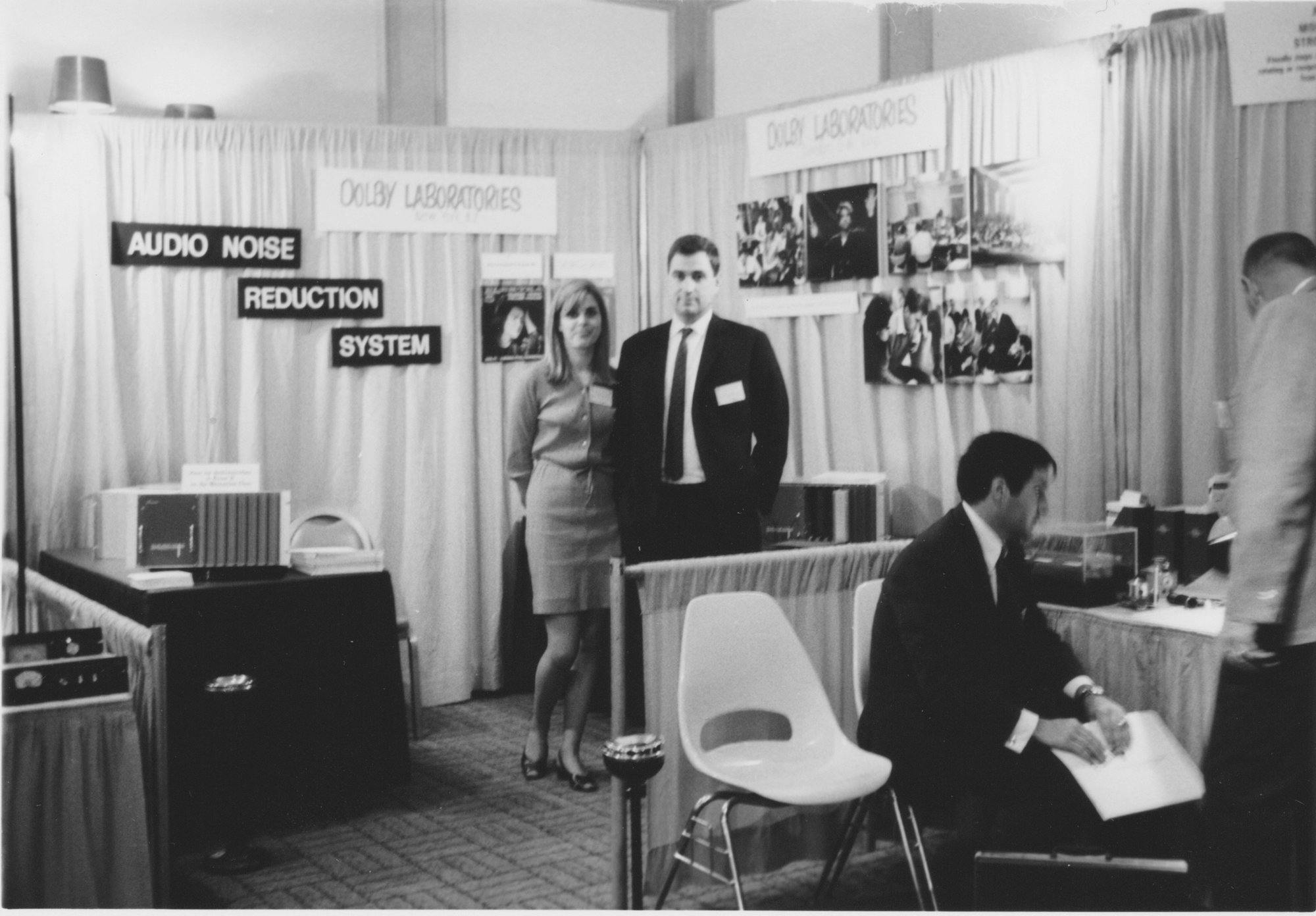 Dagmar and Ray Dolby standing next to each other in room with temporary partitions labeled Dolby Laboratories.