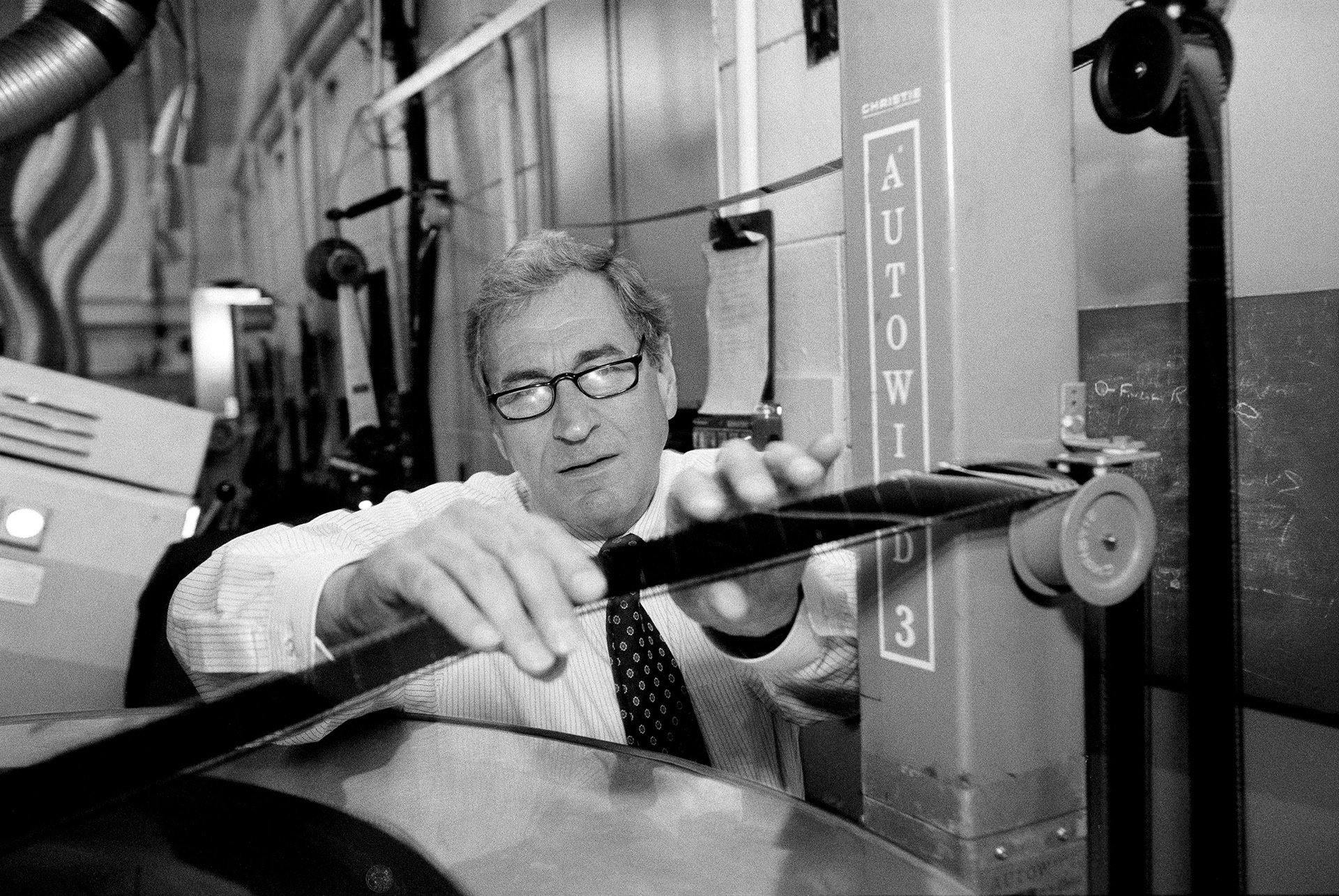 Ray Dolby wearing eye glasses in a shirt and tie inspecting  a 70 mm optical sound track.