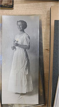 Archived black and white photo of a smiling young woman in a white, floor-length dress.