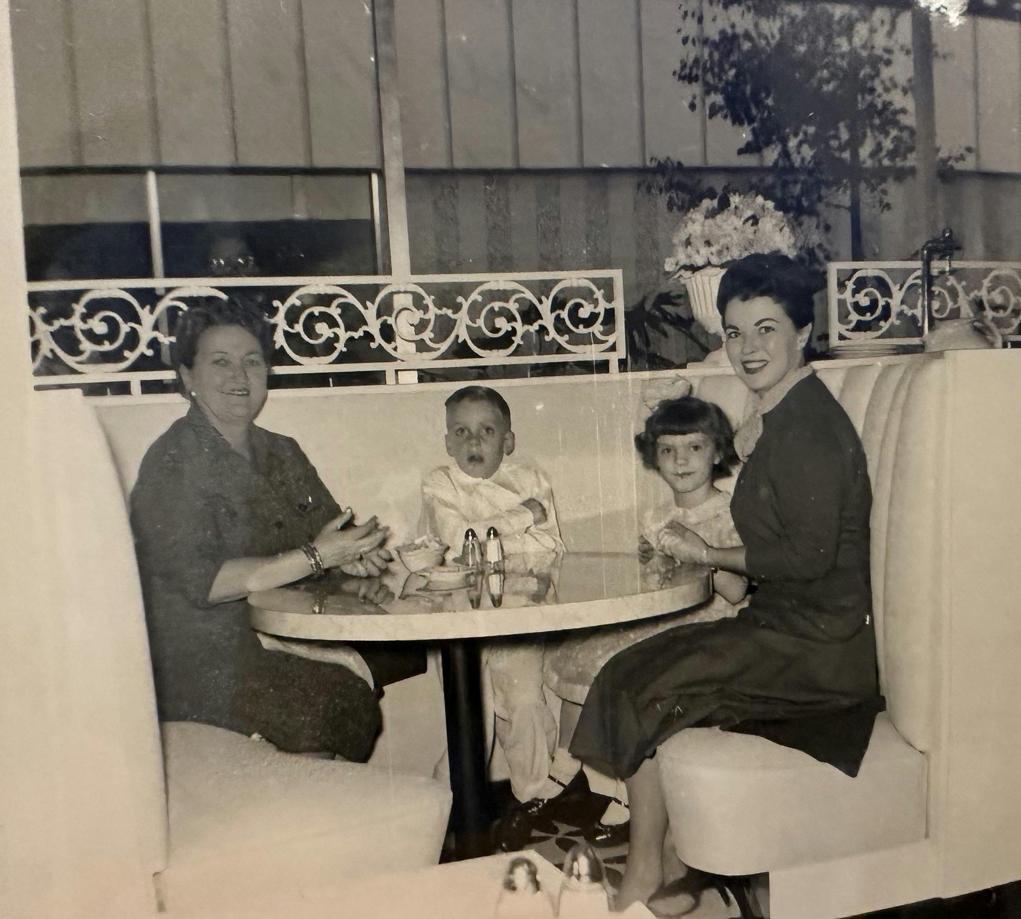 Shirley Temple Black, seated on the right at a round dining table with two children of the Sanford Childen's Convalescent Home and an unidentified woman seated on the left.