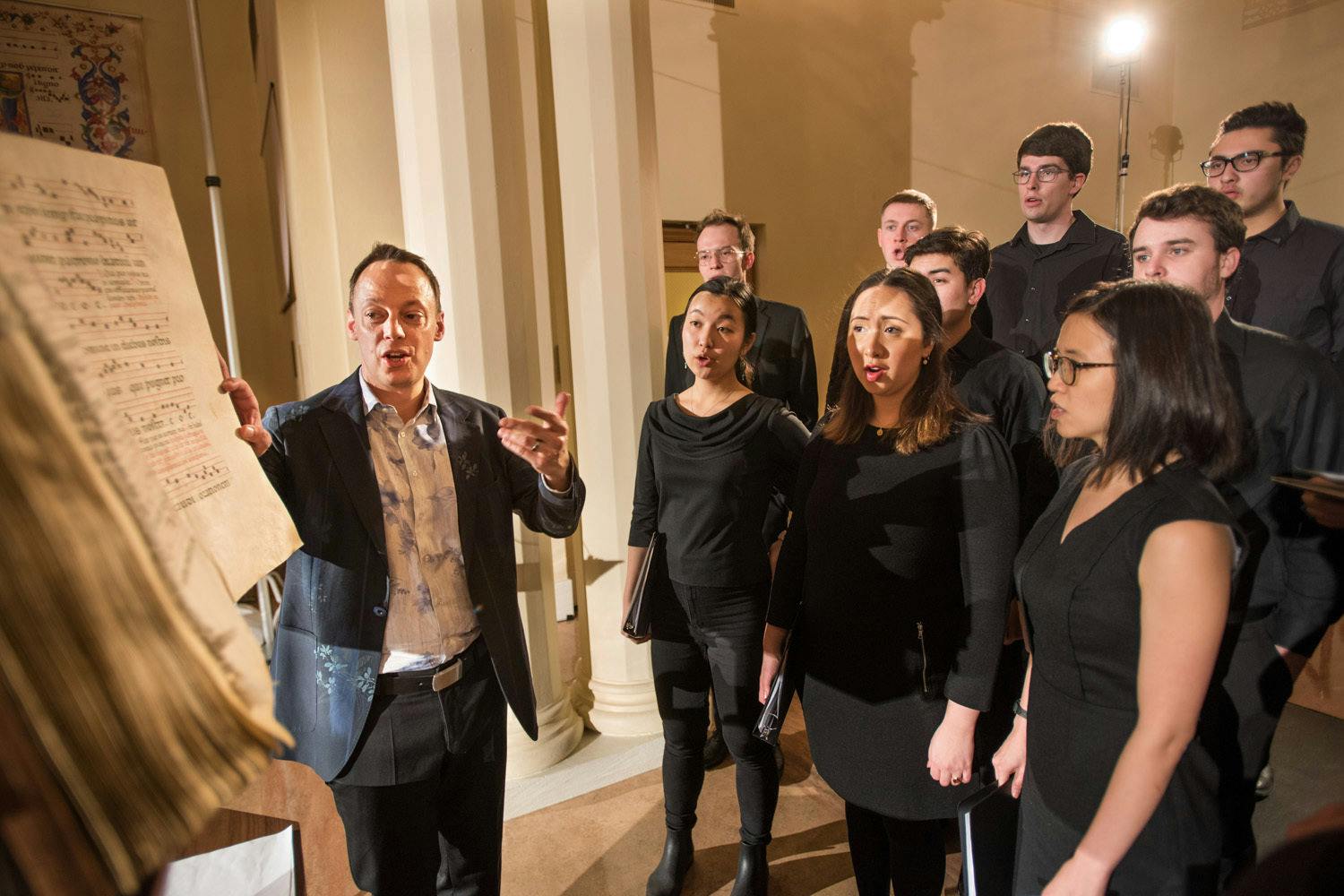 Professor Rodin leads students and members of Cut Circle in song for the opening of The Illuminated Page. Rodin stands with a page opened in the score in front of a group of eight students.